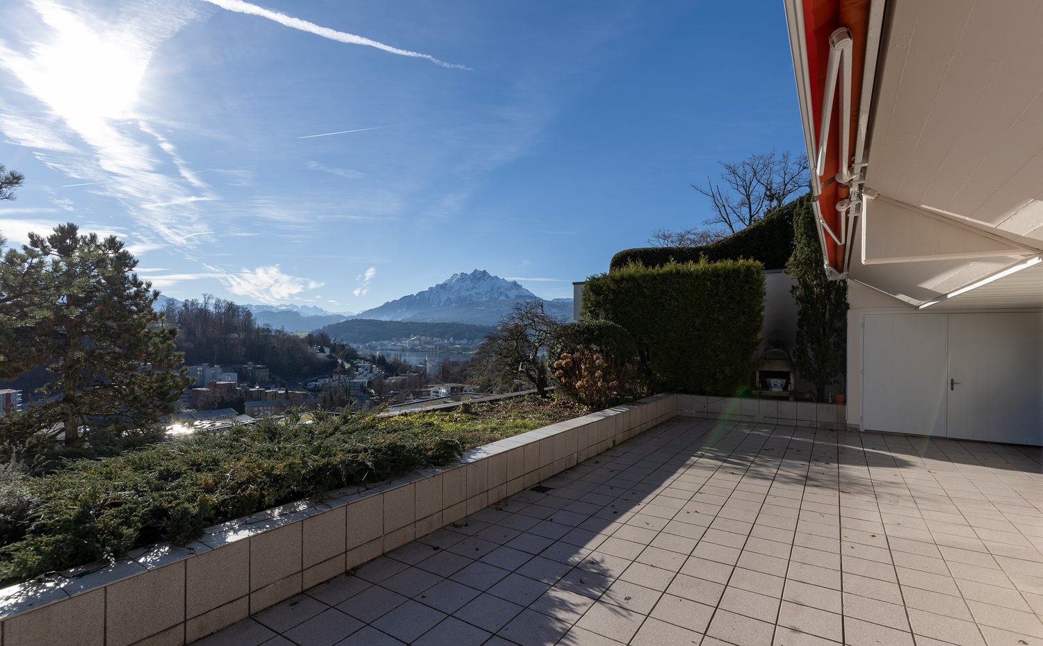 Outdoor terrace with tiled flooring, surrounded by greenery and a view of the mountains.