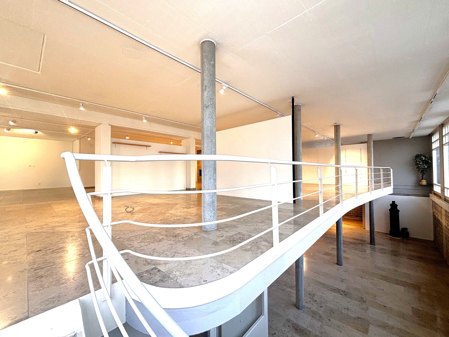 Empty room with concrete floor, white railing on the second floor, several pillars, lamps on the ceiling