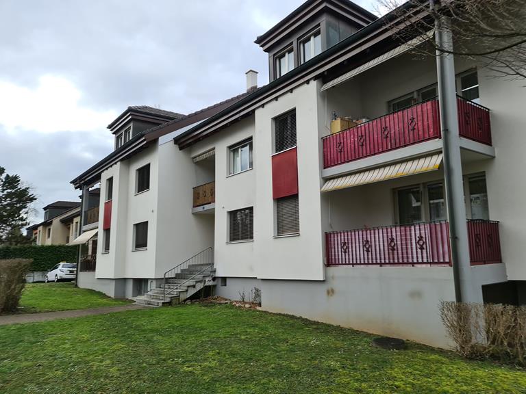 Multi-story apartment building with white exterior walls, red and yellow accents, and balconies with red railings.