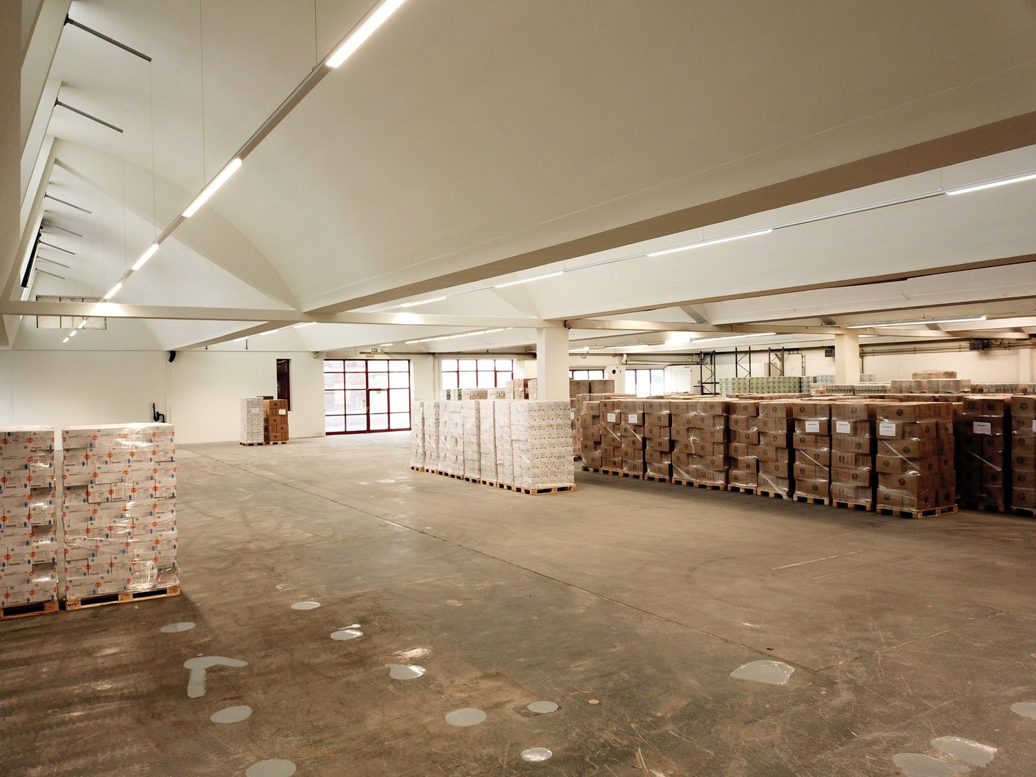 Large warehouse space, high ceilings, pallet racking, stackable boxes, white walls, white lighting, white floor