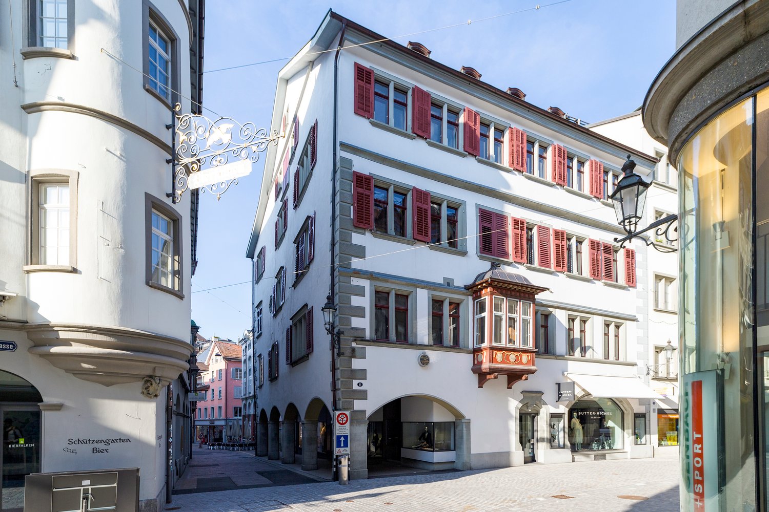 Three story commercial building, red shutters, central arched entrance, shops on the ground floor