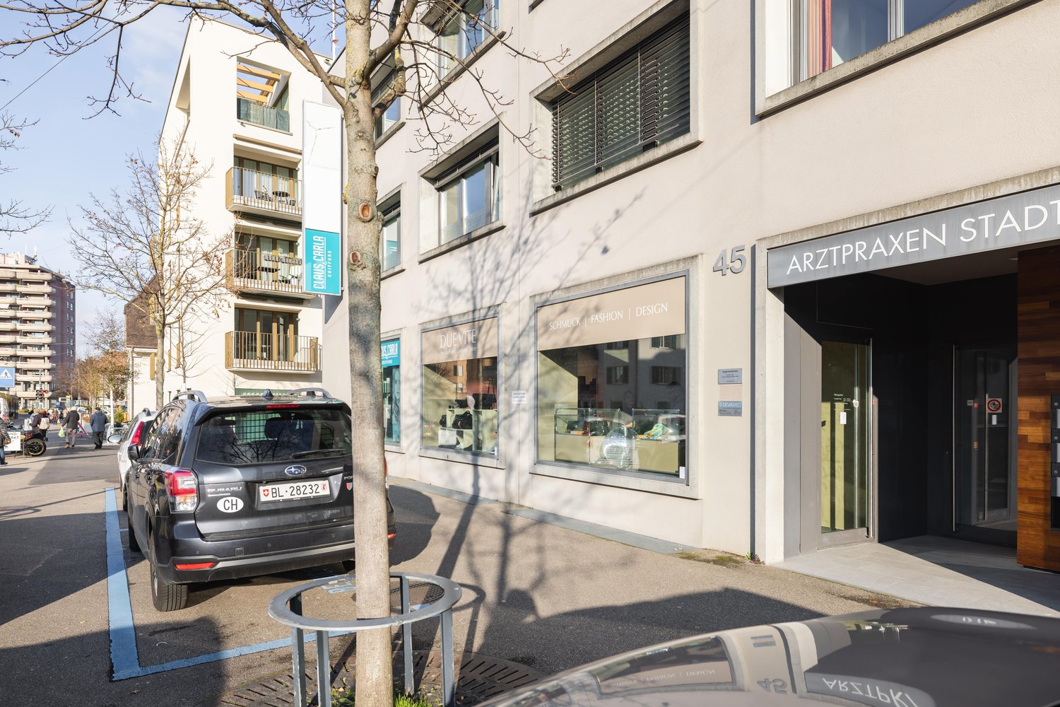 Two-story residential building, modern design, shops on the ground floor, balcony on the upper floor, white facade, parking space