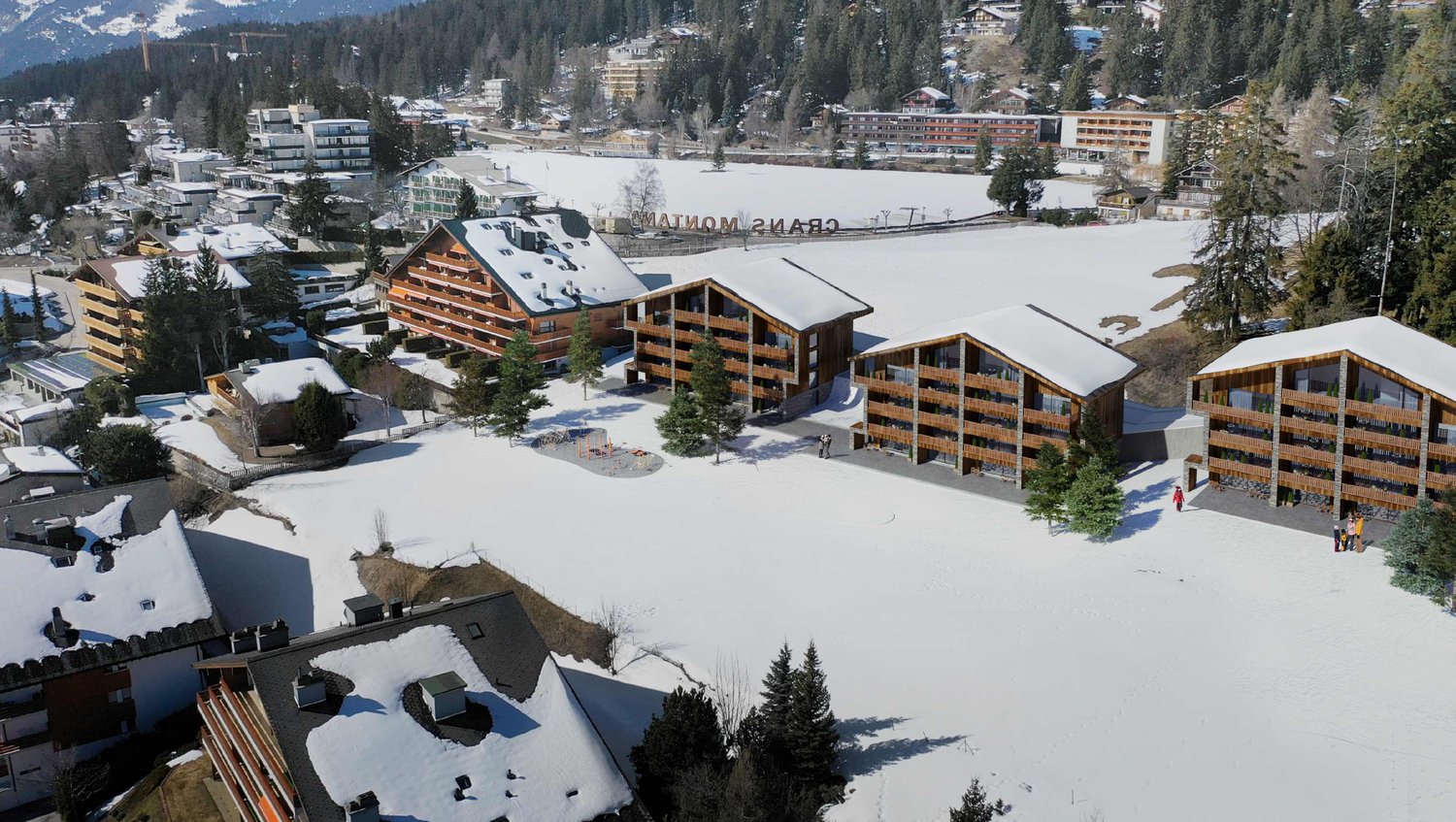 The image shows a ski resort in a snowy, mountainous landscape. There are several multi-story buildings with wooden exteriors, likely hotels or apartment buildings. The buildings have balconies and terraces. The resort appears to be located near a frozen