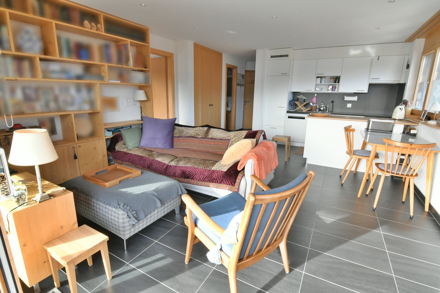 living room with sofa, coffee table, bookshelves, dining table, chairs, lamps, kitchen, cabinets, microwave