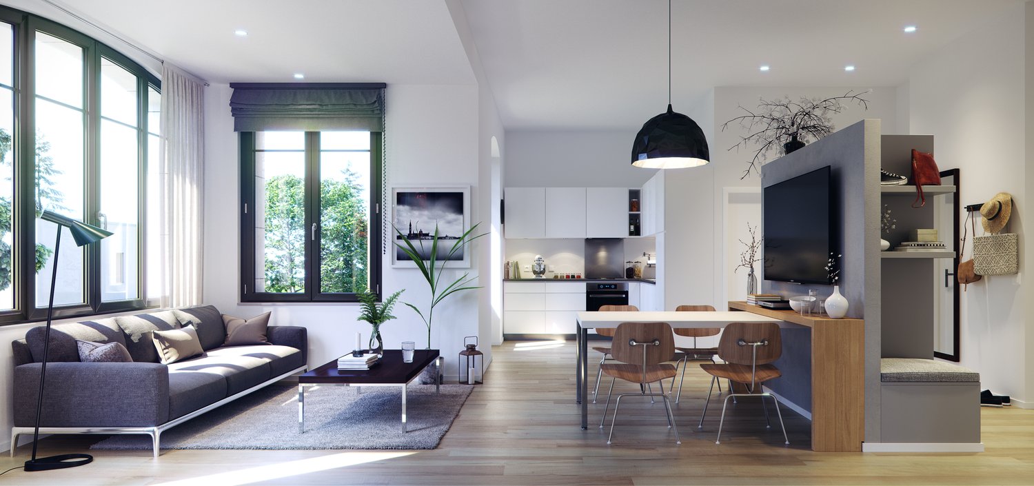 Open-concept living room and kitchen with large windows, gray sofa, wooden dining table and chairs, kitchen with white cabinets and appliances, black pendant light, and a plant decoration.