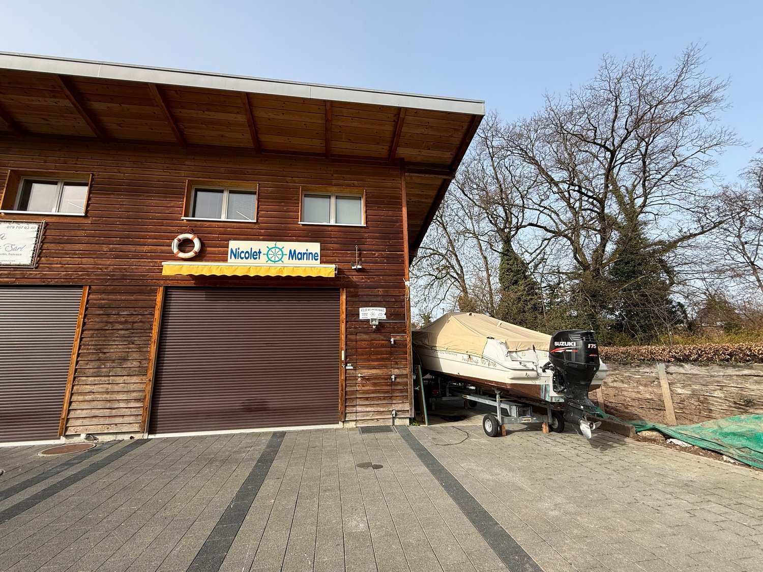Wooden building with 2 garages, sign reading Nicolet Marine, boat with an outboard motor