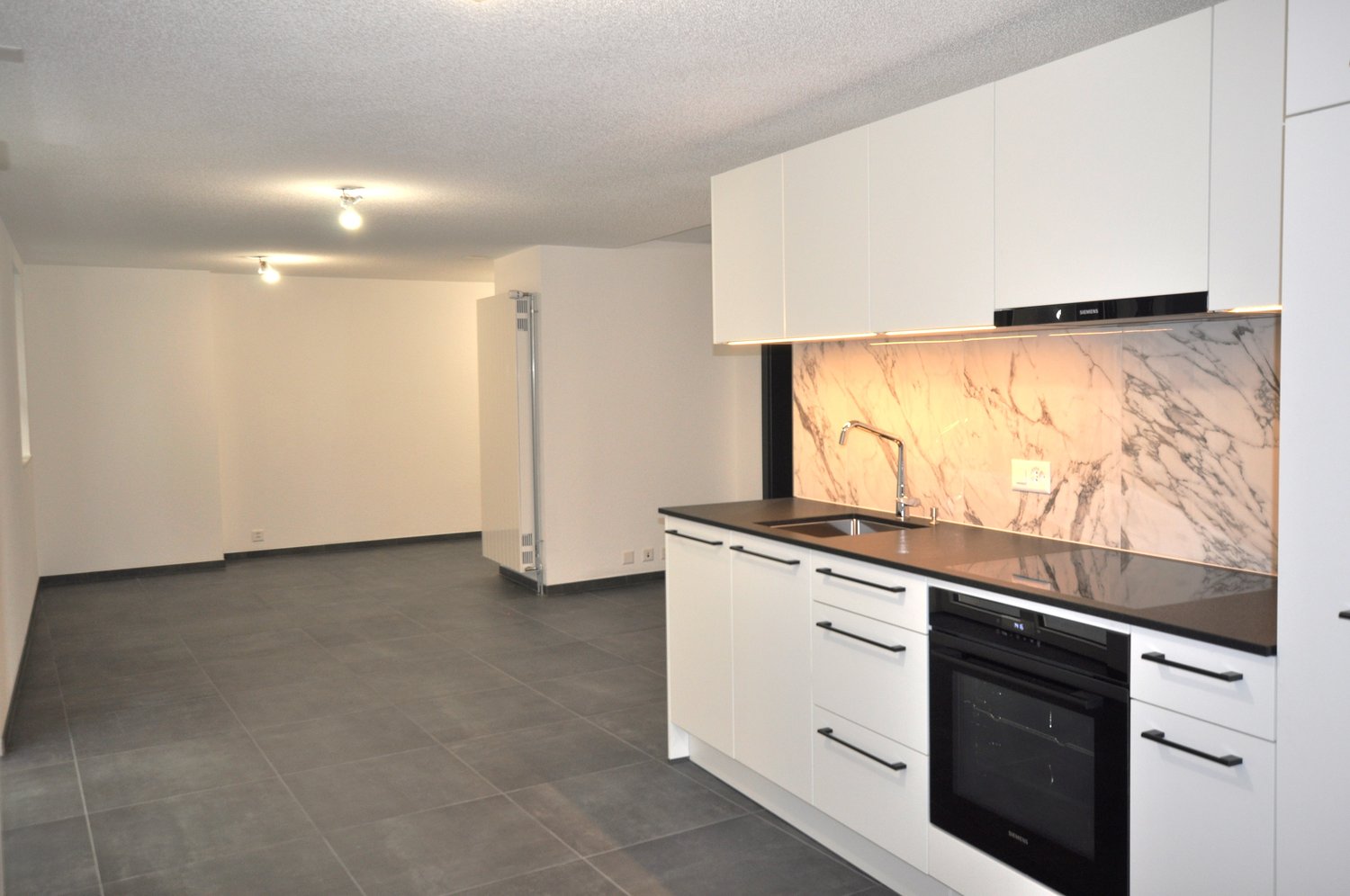 empty kitchen with white cabinets, tiled floor, sink, oven, large fridge