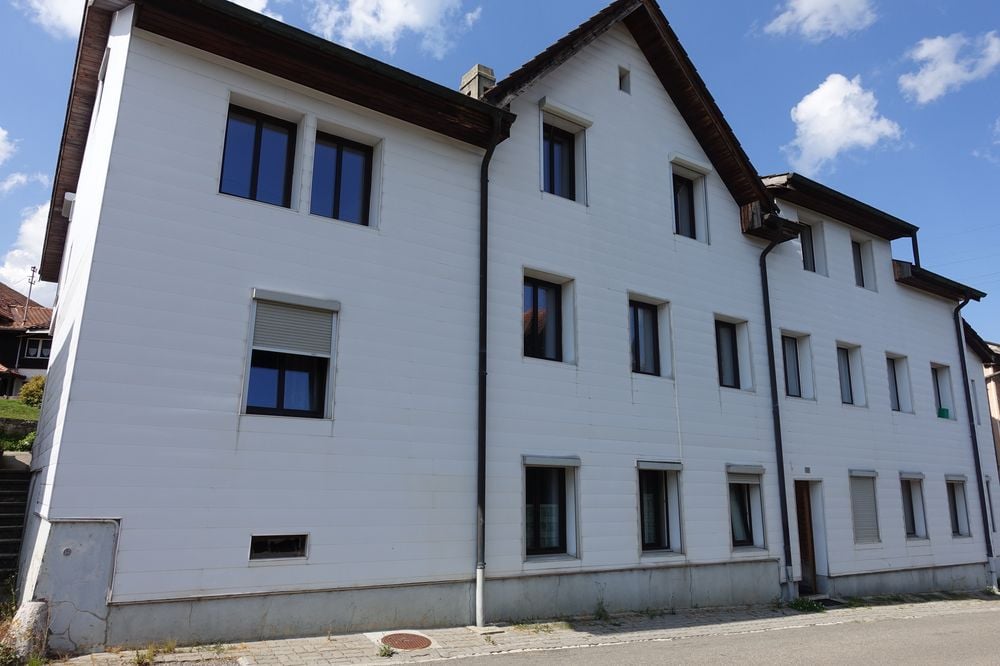 3 story residential building, white facade, multiple windows, brown roof, brick path in front
