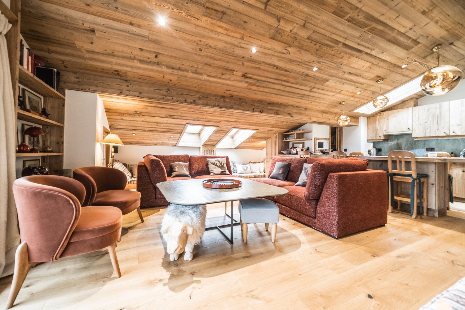 room features wooden ceiling and hardwood floors, couch with pillows, table, chairs, kitchen and dining area visible in the background