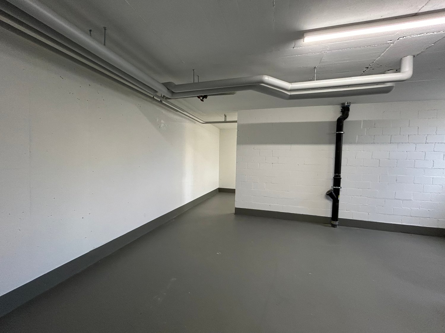 Empty room with white walls, gray floor, and visible pipes and a pipe on the wall