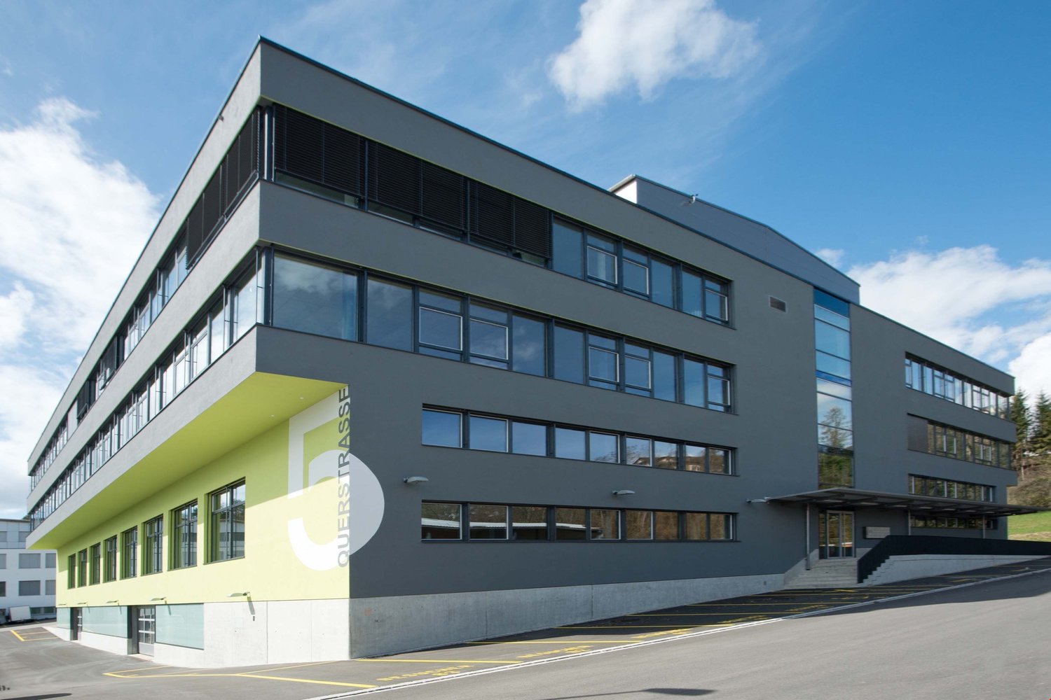 modern office building, gray exterior, glass windows, yellow accents, parking lot