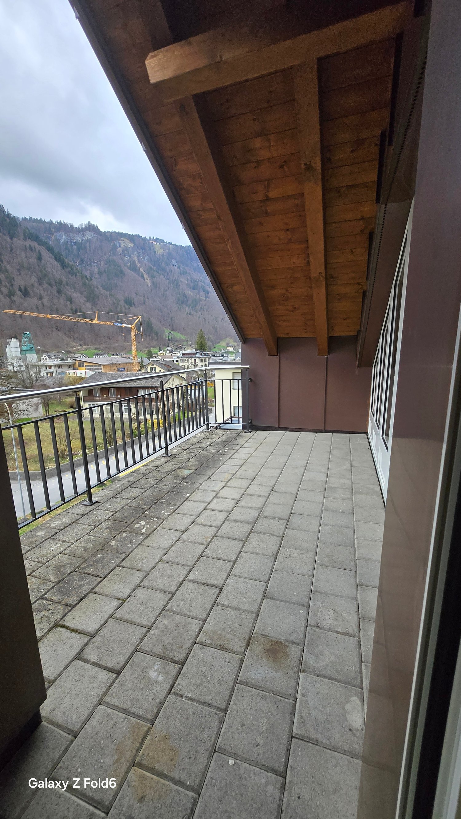 balcony with tiled floor, wooden ceiling, metal railings, view of mountains and buildings