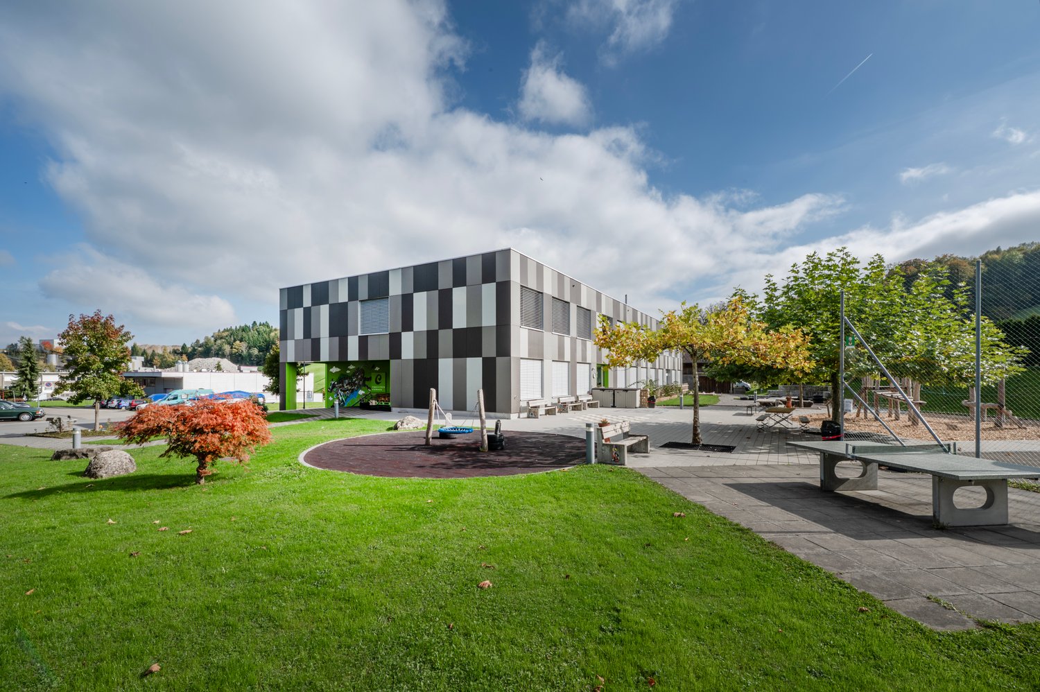 Modern architectural building with checkered facade, located outdoors, surrounded by a lawn, playground, and trees.