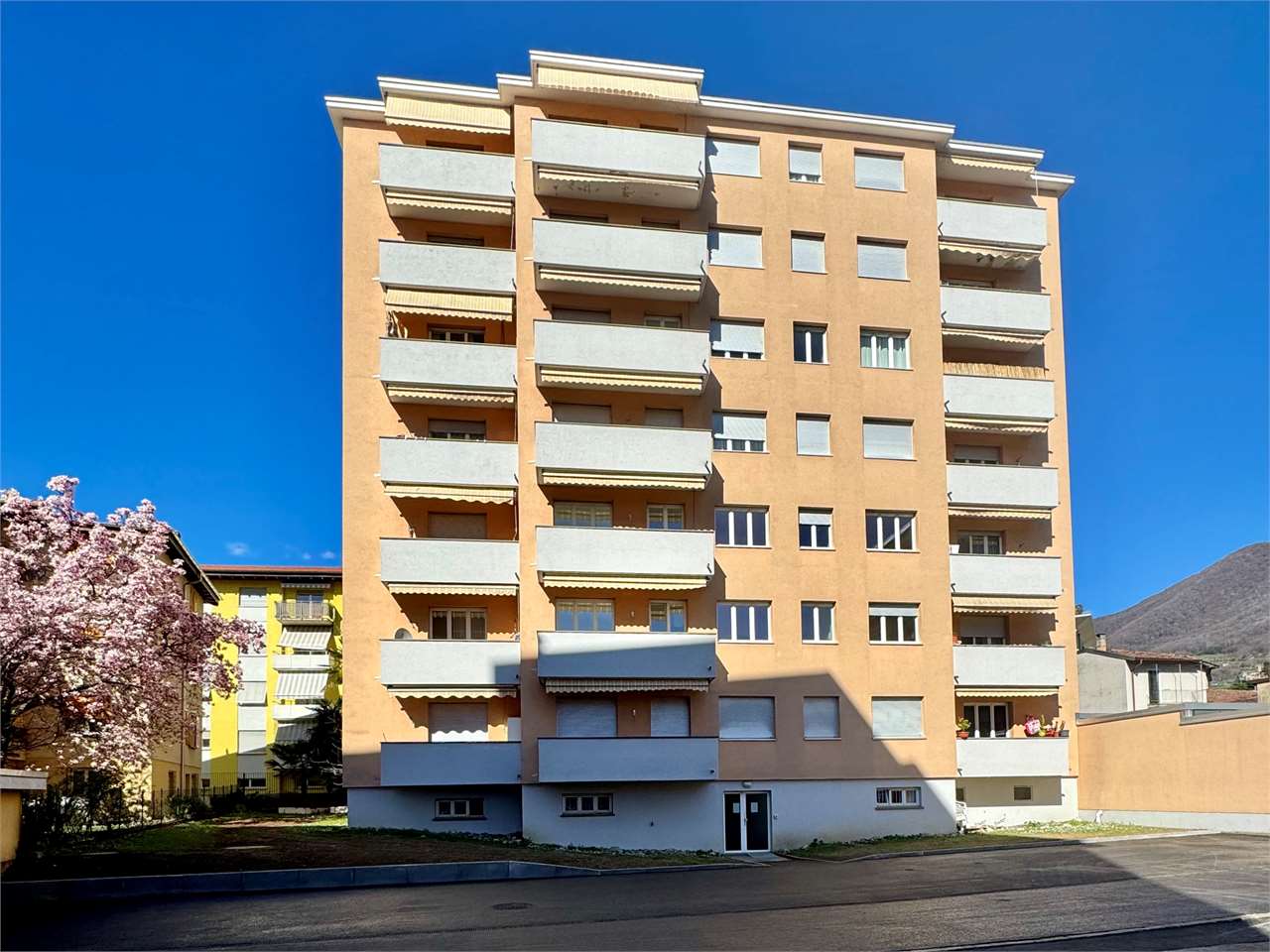 Multi-story apartment building, balconies, large windows, main entrance, exterior parking