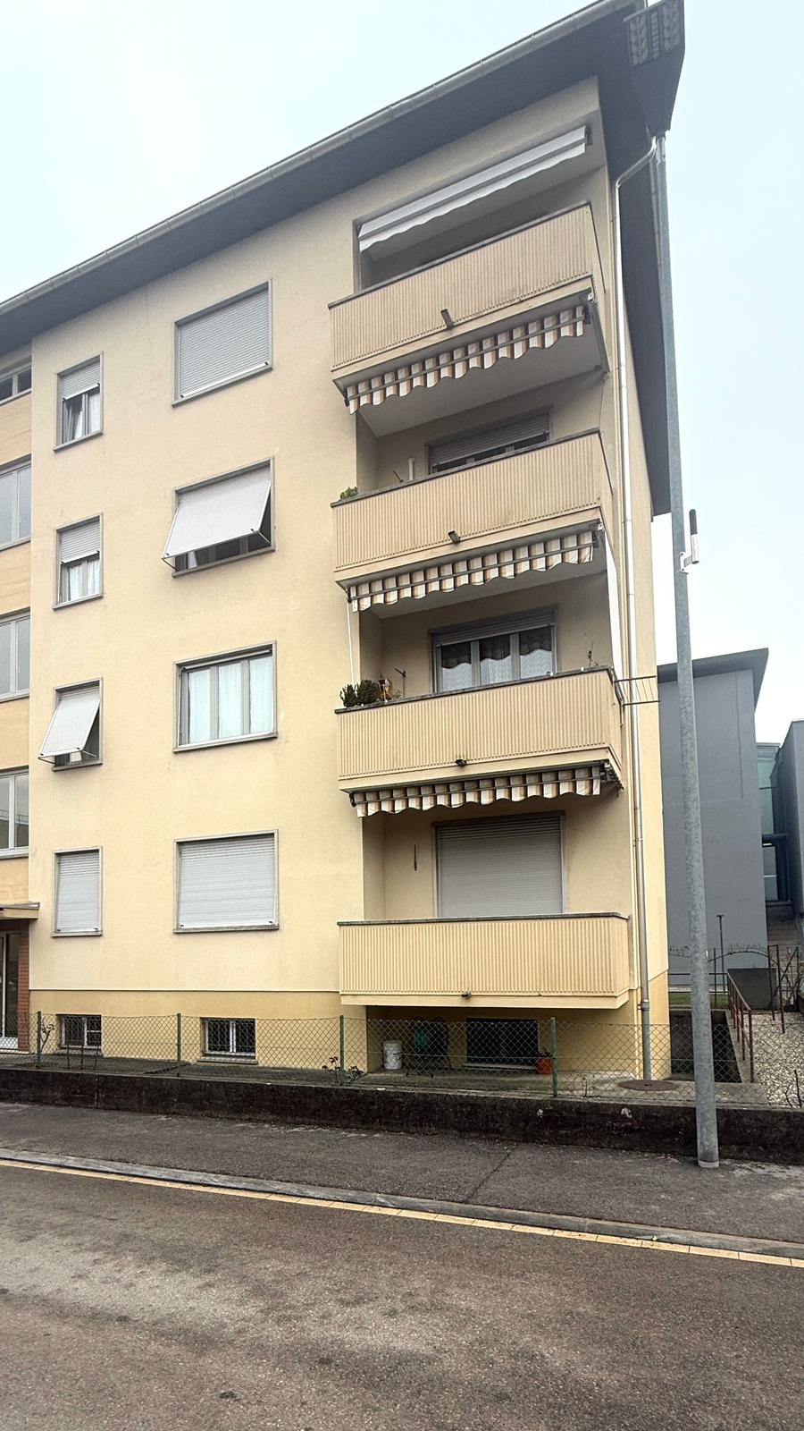 Multistory apartment building, balconies, yellow exterior, white window shutters, greenery