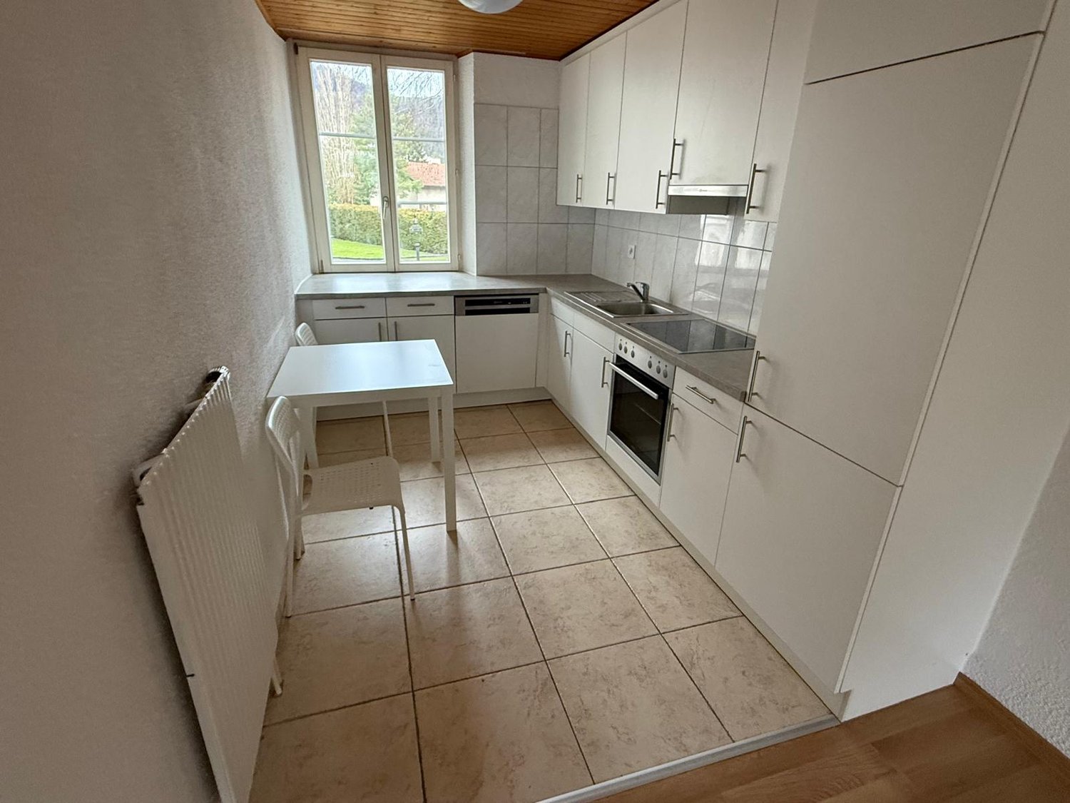 white cabinets, tile floor, white table and chairs, large window, gas stove, sink, dishwasher, heating unit
