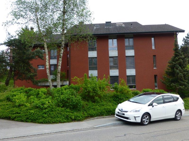 red brick building, 3 stories, white framed windows, balconies, greenery