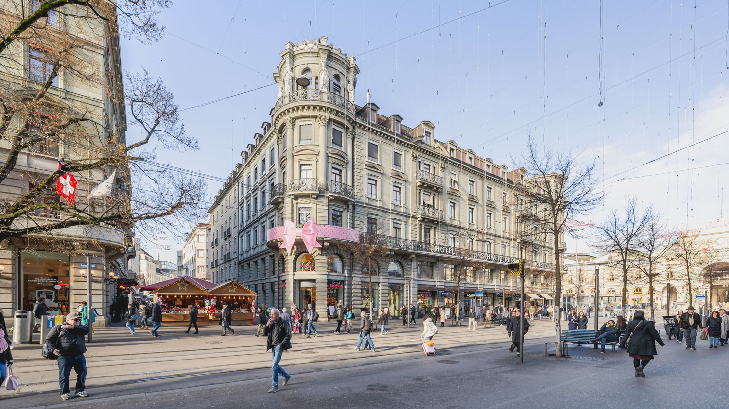 large building, multiple windows, pink bow on the front, many people walking around