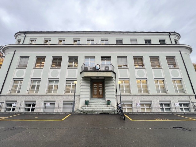 large building, white exterior, multiple windows, central entrance with stairs, bicycle parked in front