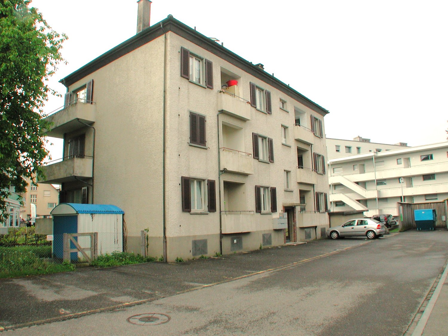 4 story building, balconies, parking lot, small shed