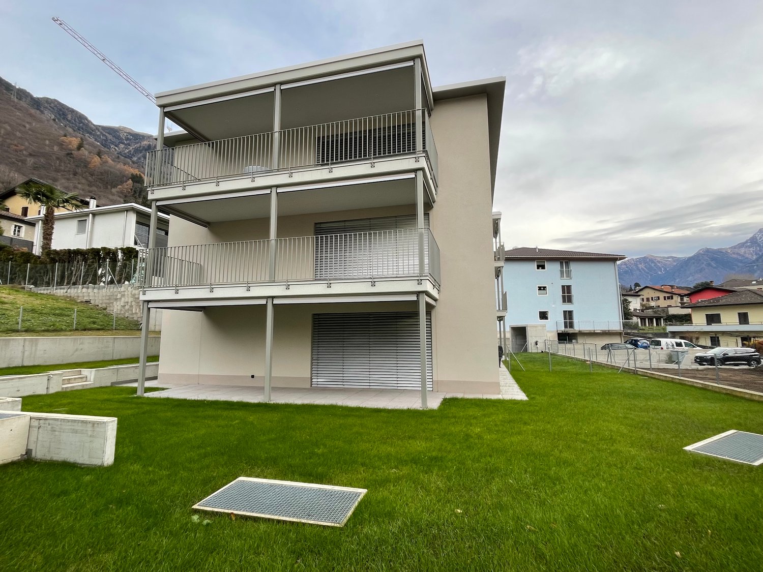 3-story modern apartment building with balconies, garage, and grassy lawn area in front