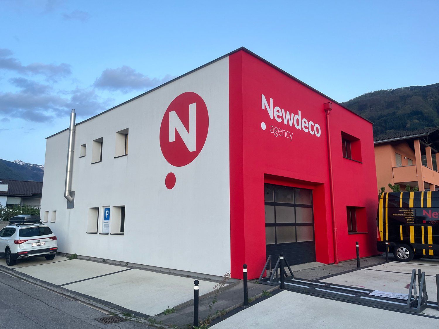 Commercial building, red and white wall, large window, 3rd floor, car parked, mountains in background
