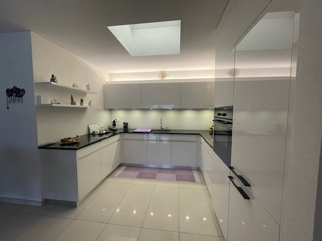 modern kitchen, white cabinets, white tiled floor, black countertops, stainless steel appliances, skylight