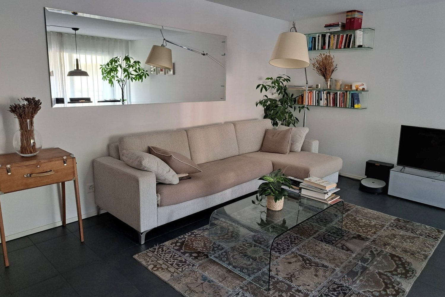 Living room with a beige sofa, glass coffee table, carpet, and a large mirror on the wall.