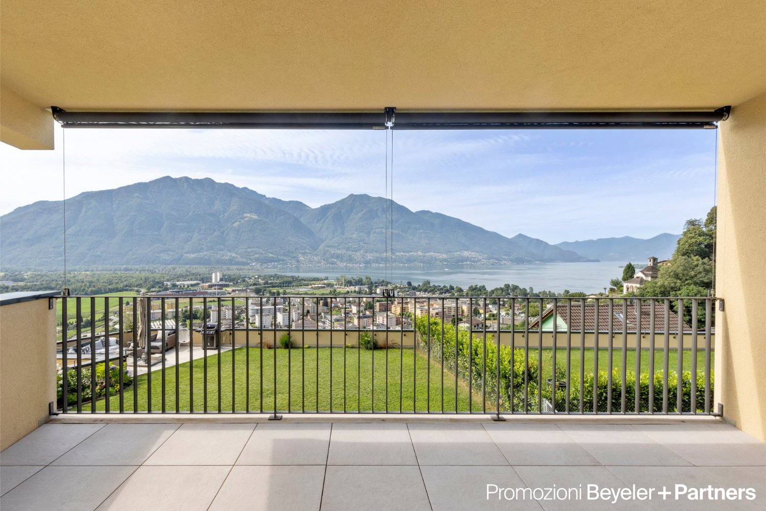 large glass walls, metal railing, tiled floor, distant view of city, mountains and lake