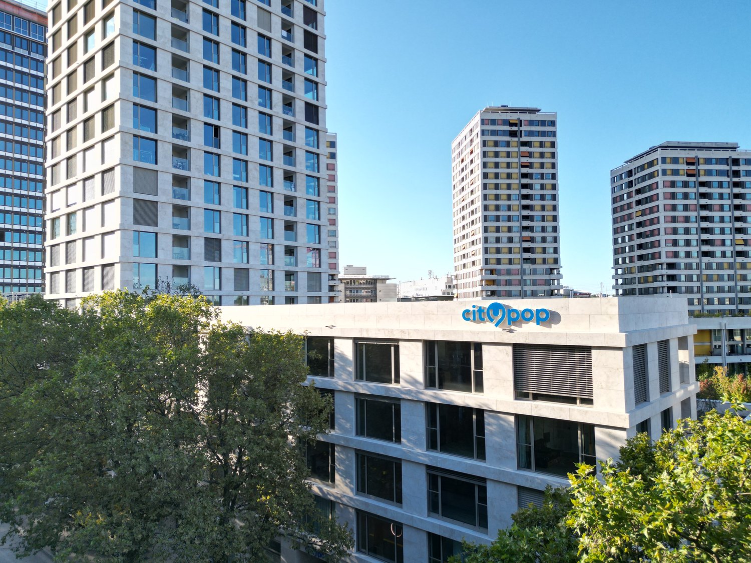 Tall modern high-rise buildings with glass facades, surrounded by trees. The building in the foreground has the 'Citypop' logo on it.