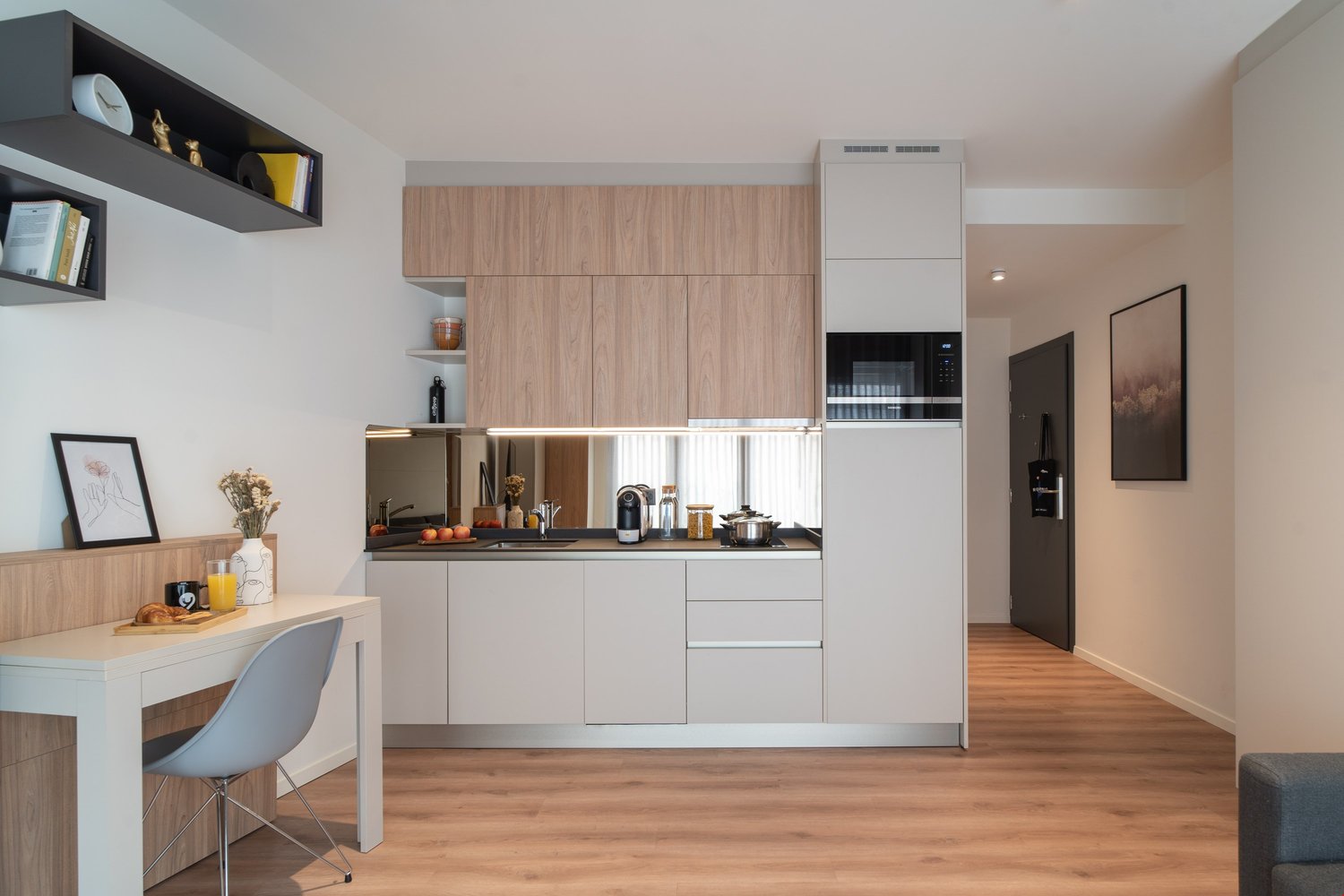 Modern kitchen with light wood cabinets, white appliances including a dishwasher, and a small dining area with a table and chair