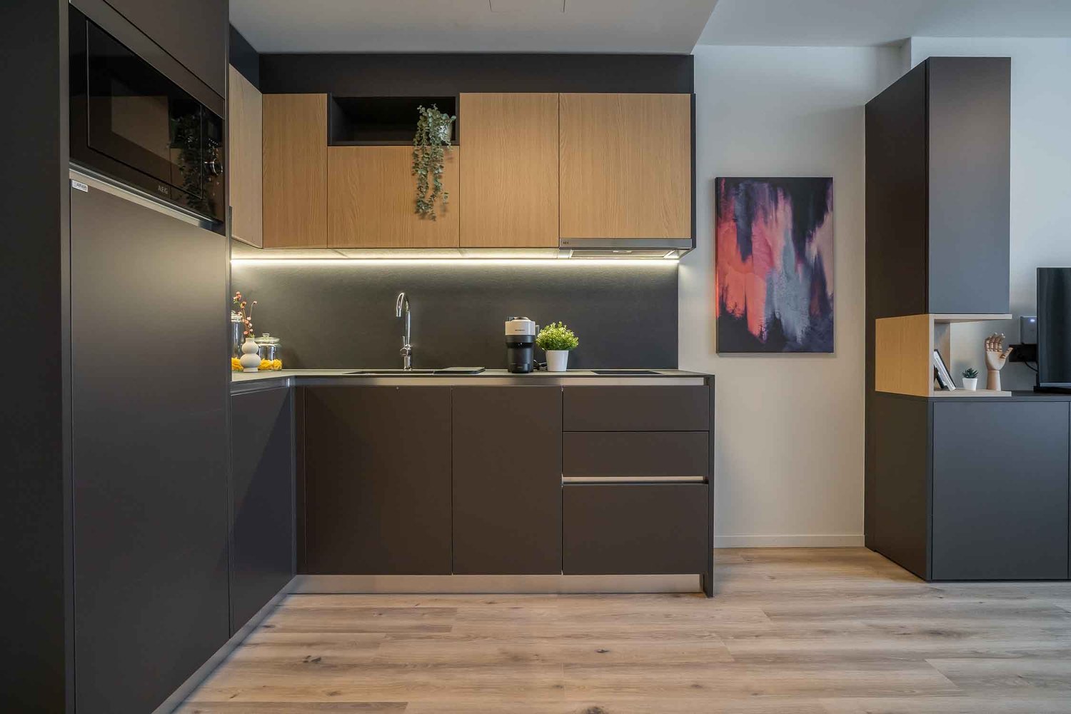 Modern kitchen with dark cabinets, wooden accents, stainless steel appliances, and a colorful abstract artwork on the wall
