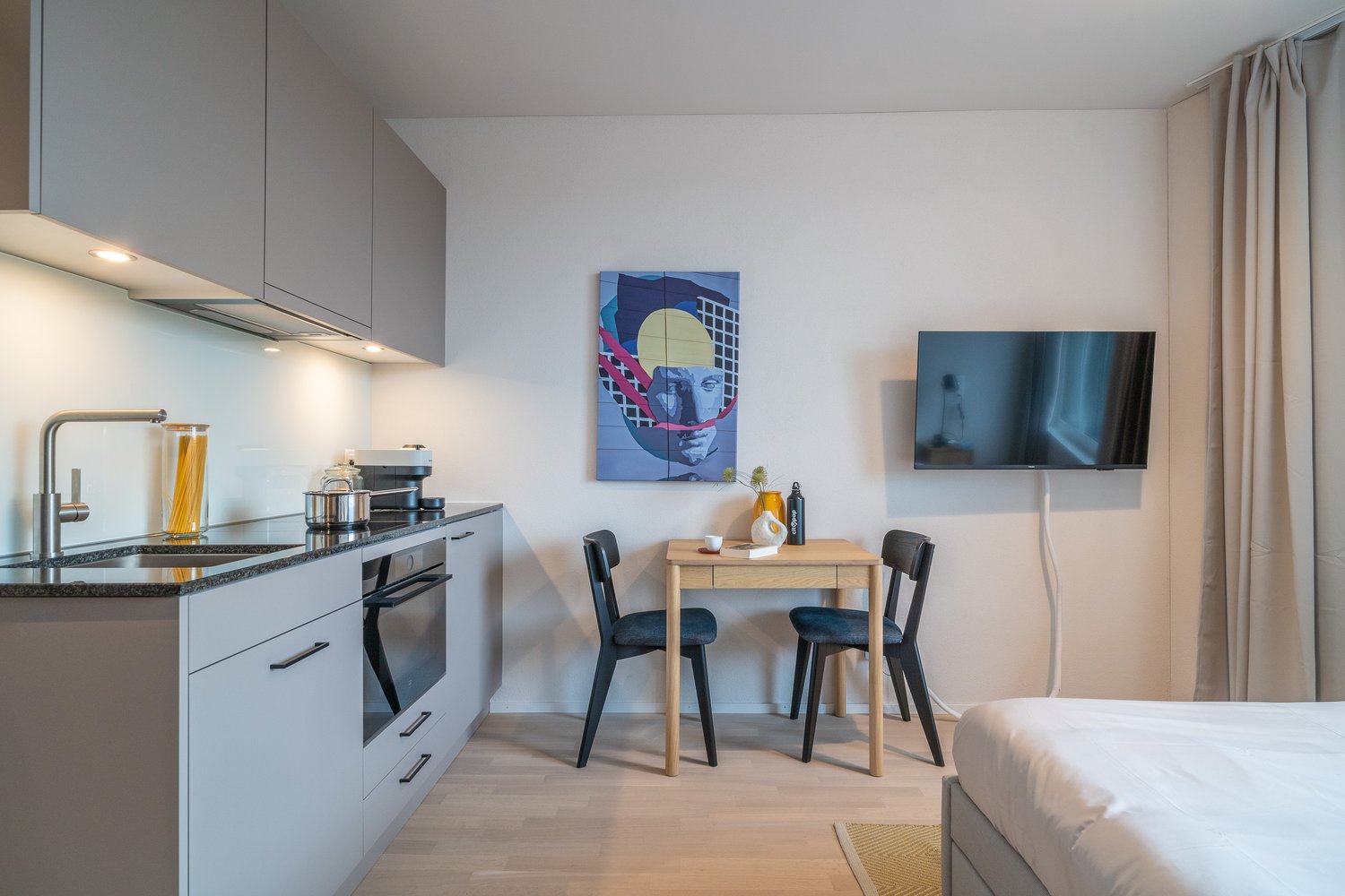 Open plan kitchen with a sink, gas stove, cabinets, microwave, and a dining table with chairs. Next to it is a bedroom with a bed.
