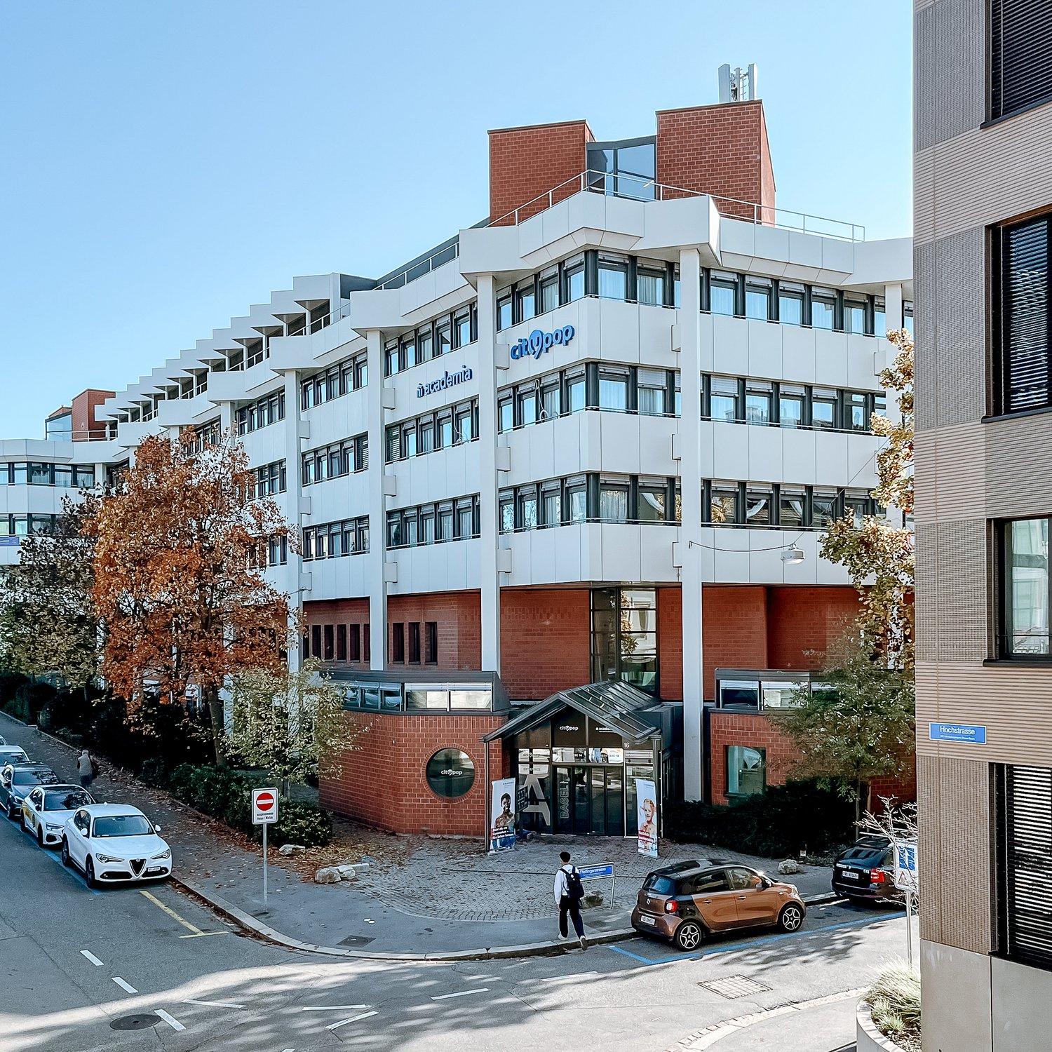 Multi-story office building with a mix of brick and glass exterior, parking spaces in front, and some trees and landscaping around the building.