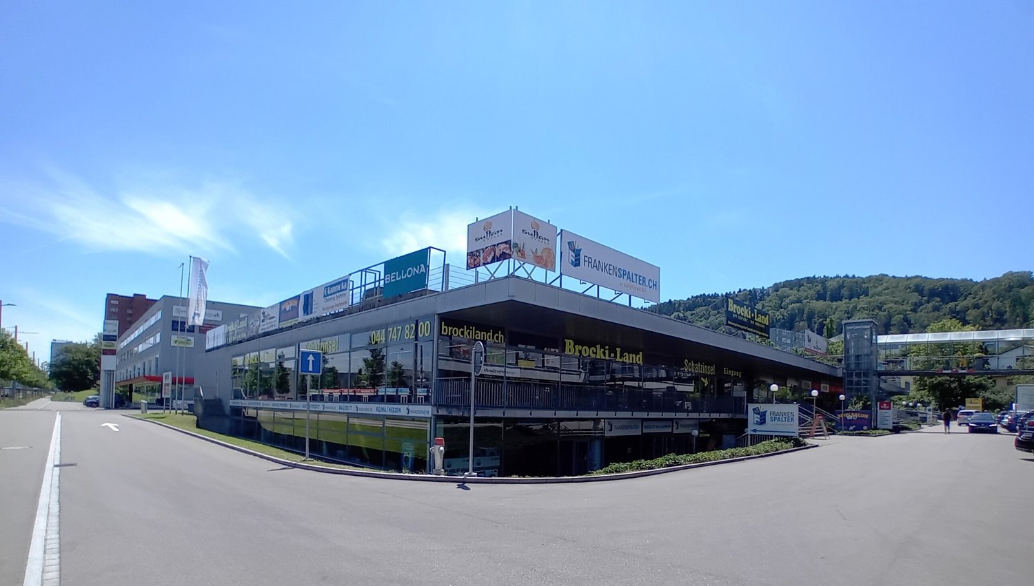 Commercial building with glass facade, multiple signs, parking lot, entrance with stairs, street lights, greenery