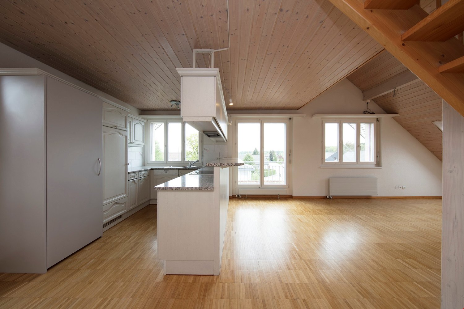 Open kitchen with island, wooden floors, white cabinets, large windows, wooden ceiling