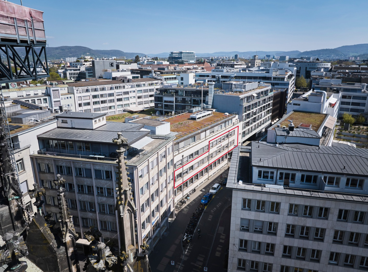 Aerial view of a city with multiple buildings, one highlighted with red lines indicating a specific building.