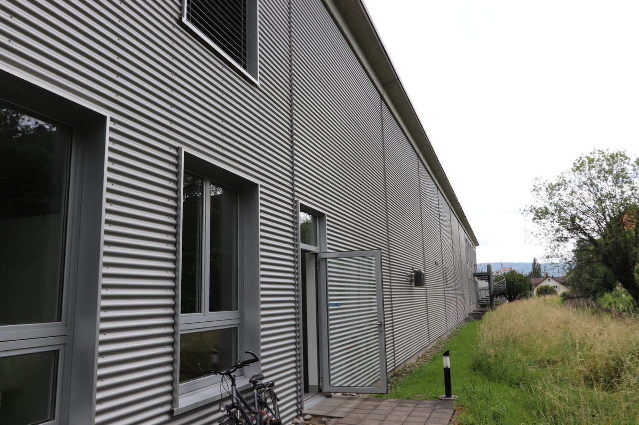 Metal cladding, glass windows, open door, bicycles, concrete path, metal pole, grassy area