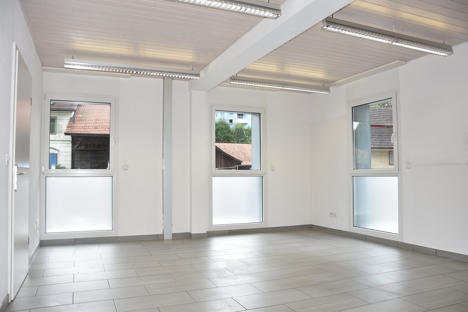 Empty room with sliding doors, windows, tiled floor, and overhead lighting.