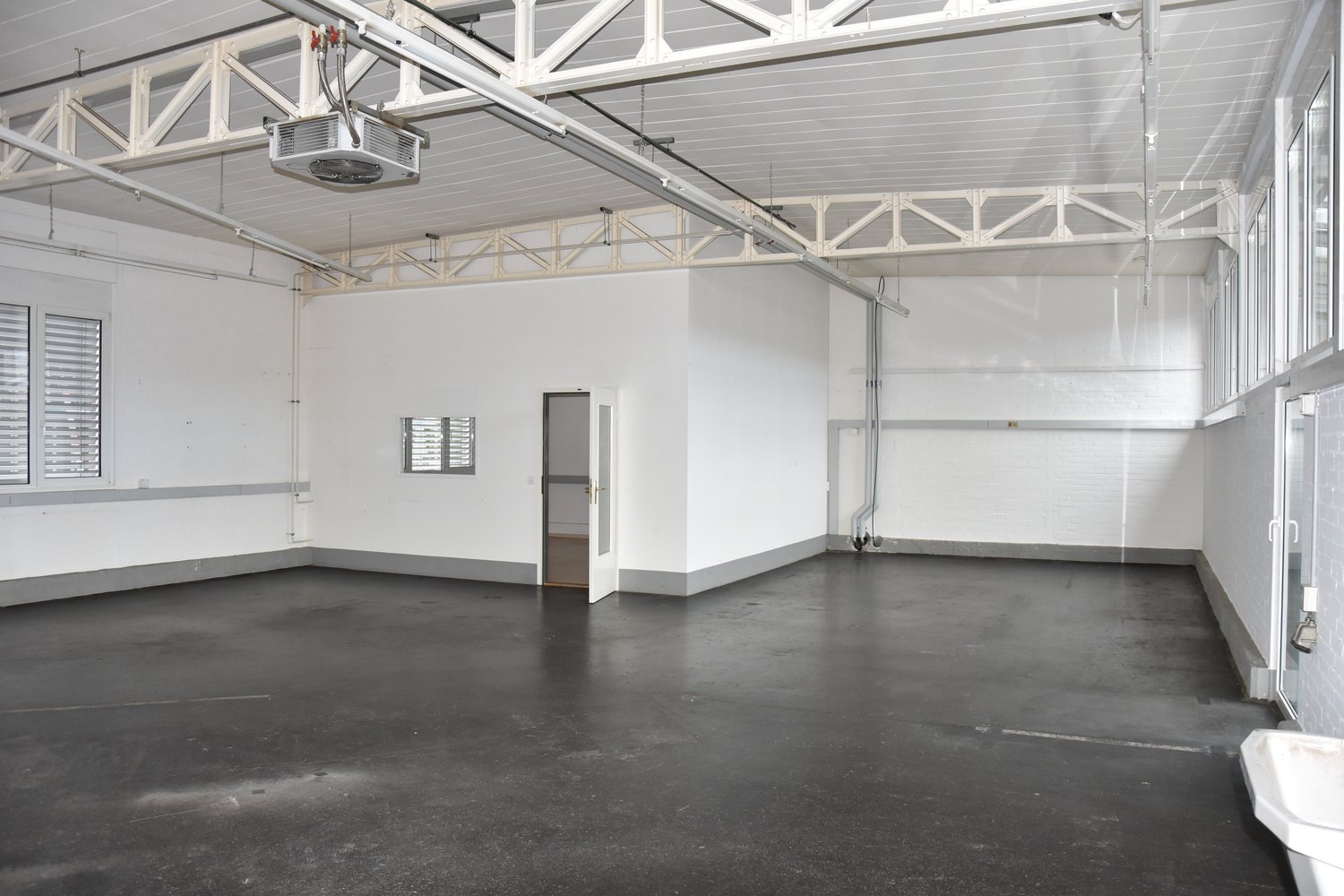 Empty room with white walls, black floor, windows, and an open door.