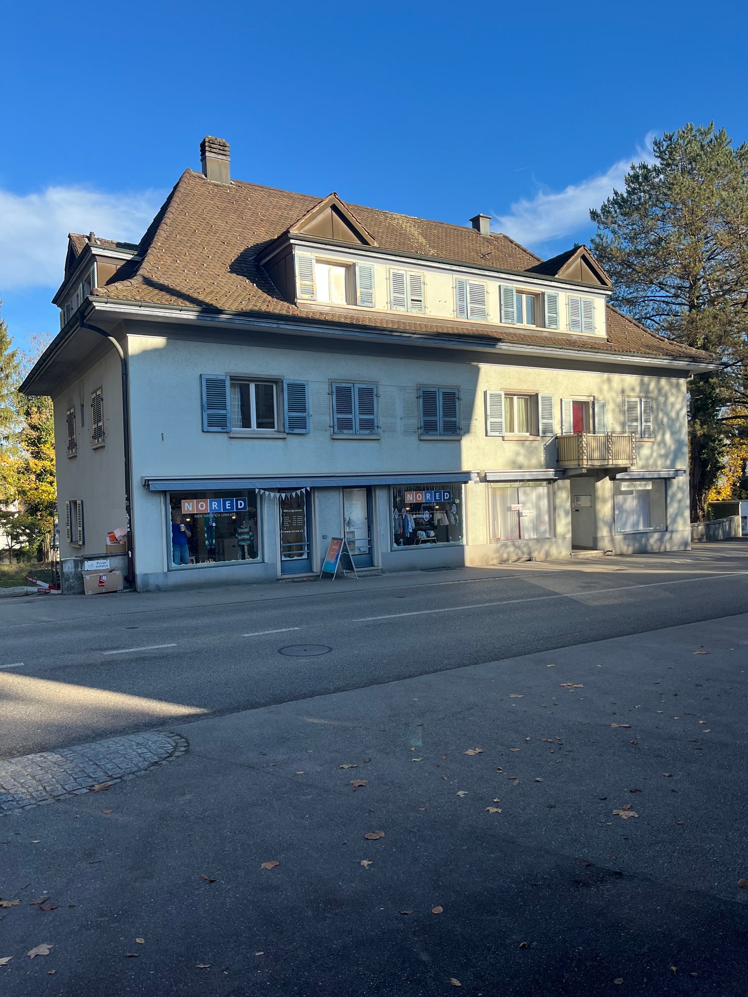 3 story house, brown roof, white walls, multiple windows, balcony, shops on the ground floor