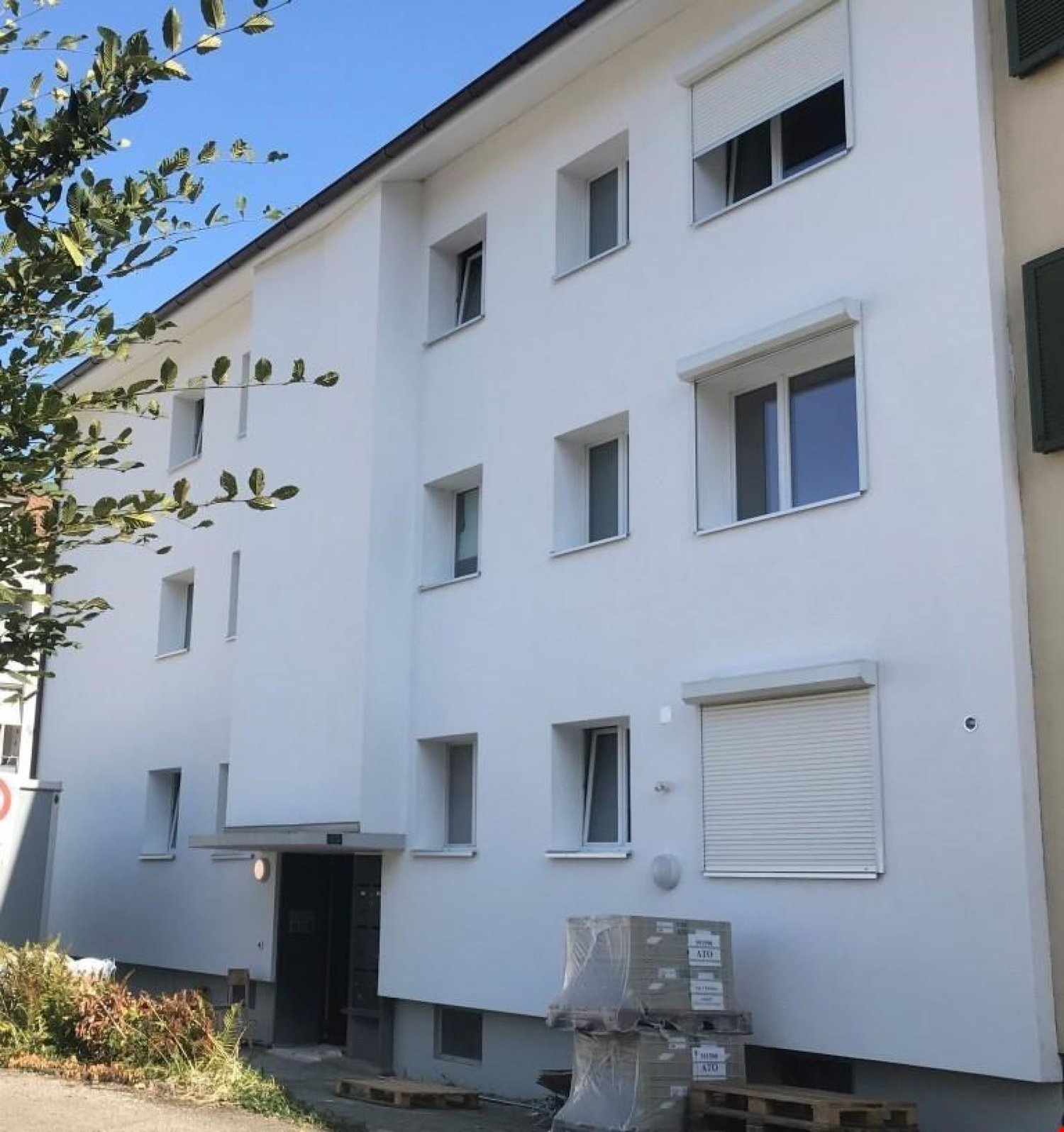 Multi-story building, white exterior, multiple windows, entrance with canopy, some items stored outside