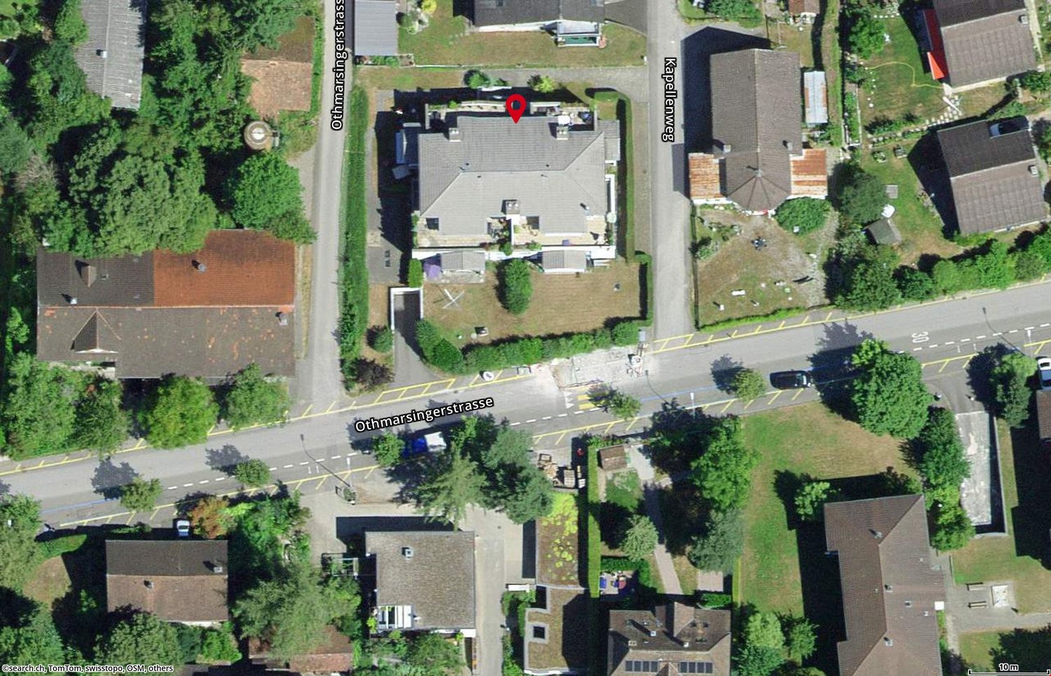 House located on a street corner, surrounded by trees and other houses, with a driveway leading to the front entrance.