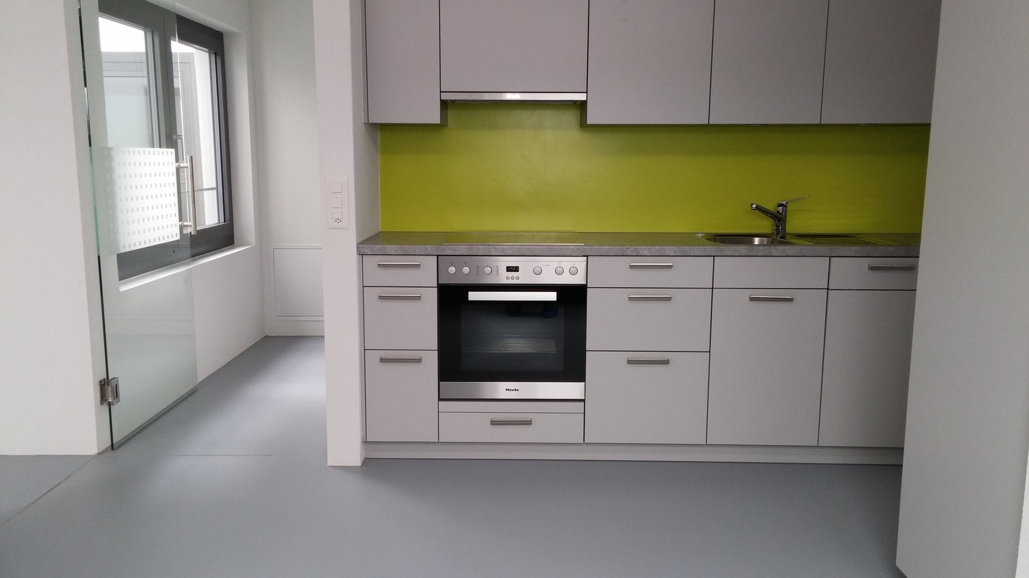 Modern kitchen with gray cabinets, green backsplash, built-in oven and dishwasher, and a sink with faucet