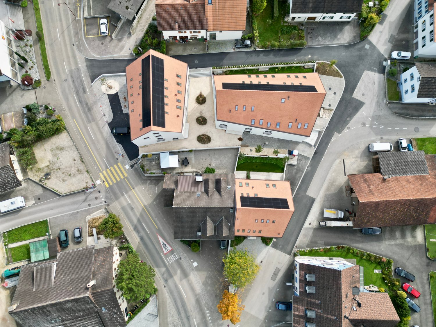 Several residential buildings at a corner, surrounded by streets, driveways, and parking areas. One building has solar panels.