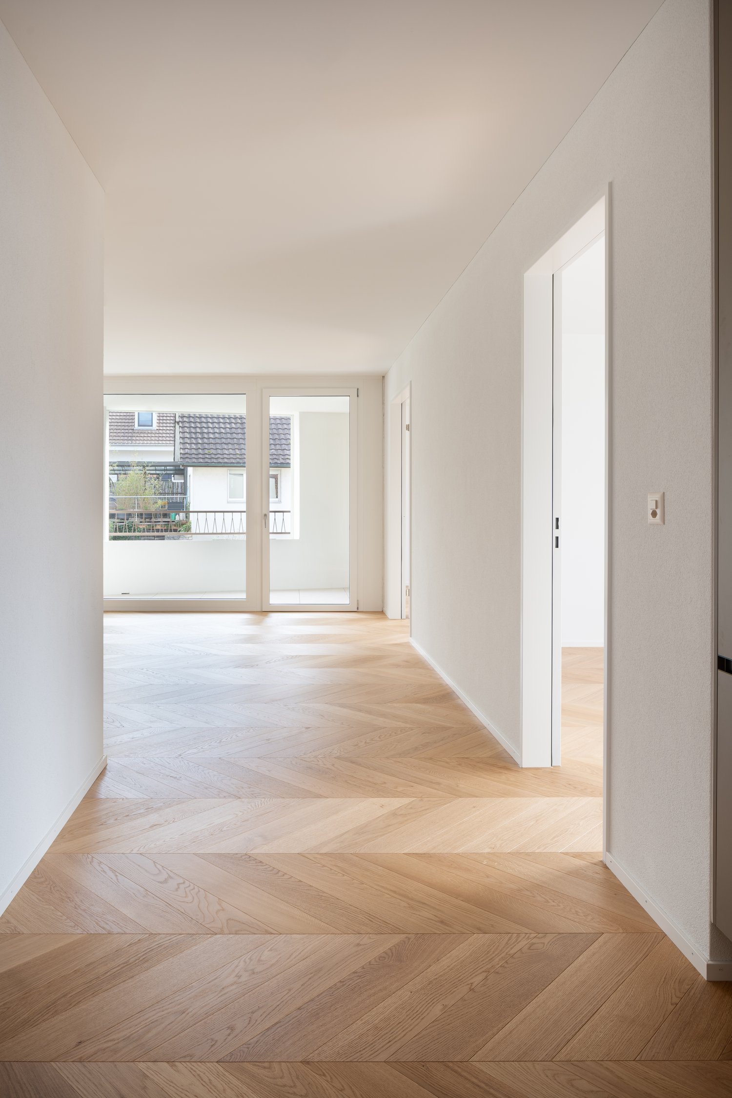 empty room, wooden flooring, sliding doors leading to a balcony, large windows, white walls