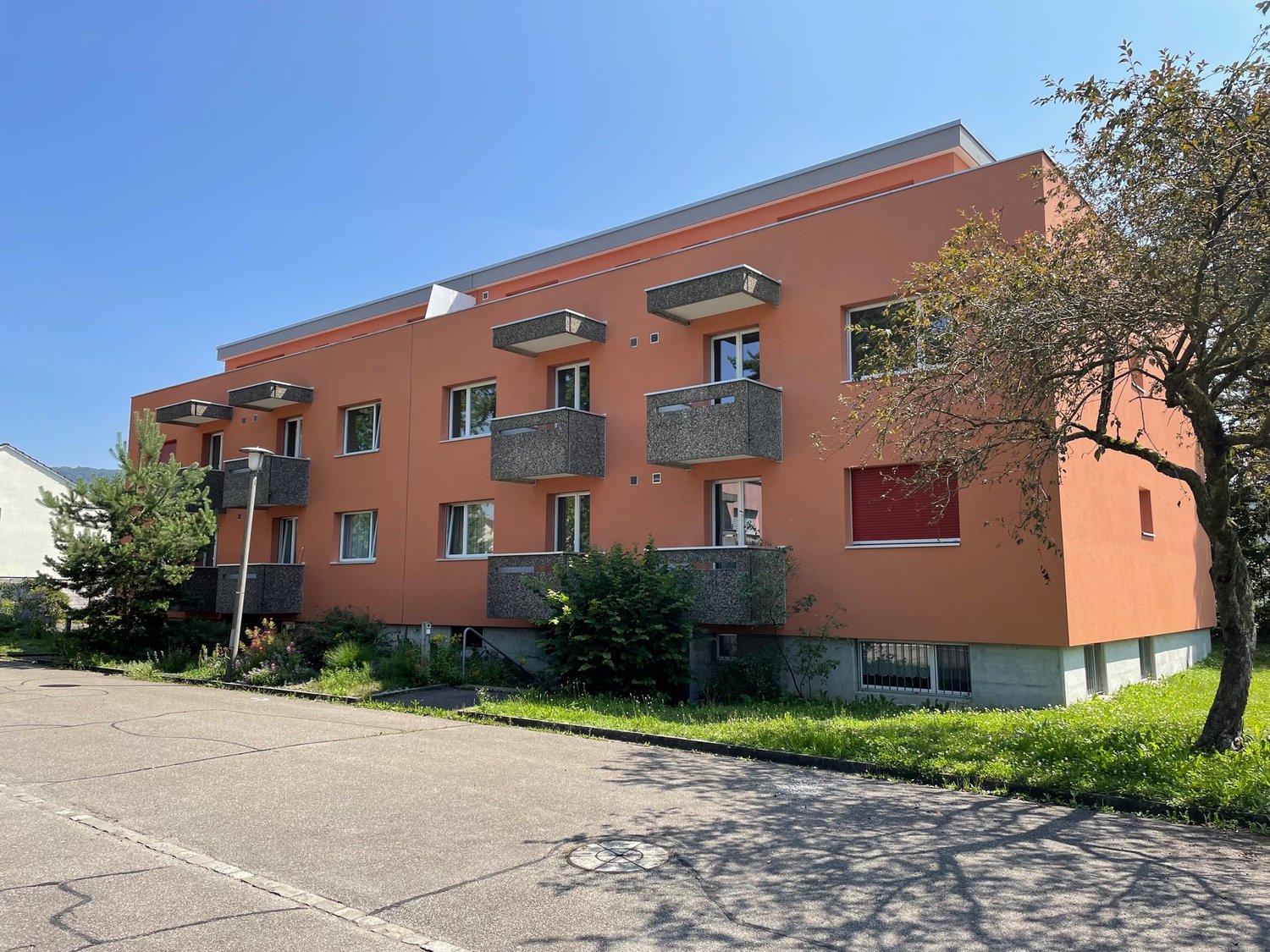 3-story apartment building, orange exterior, multiple balconies, windows, concrete base, greenery