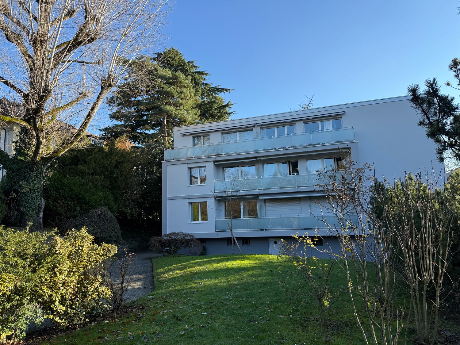 white house, several balconies, 3 floors, large windows, garden, shrubs, green grass