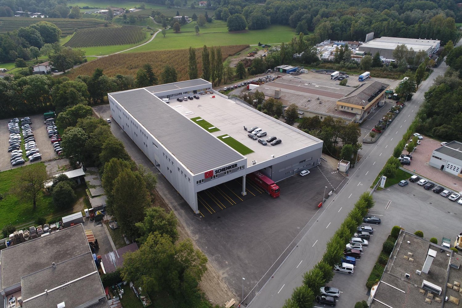 Industrial building with a car park on a landscaped plot with green spaces, located near a road