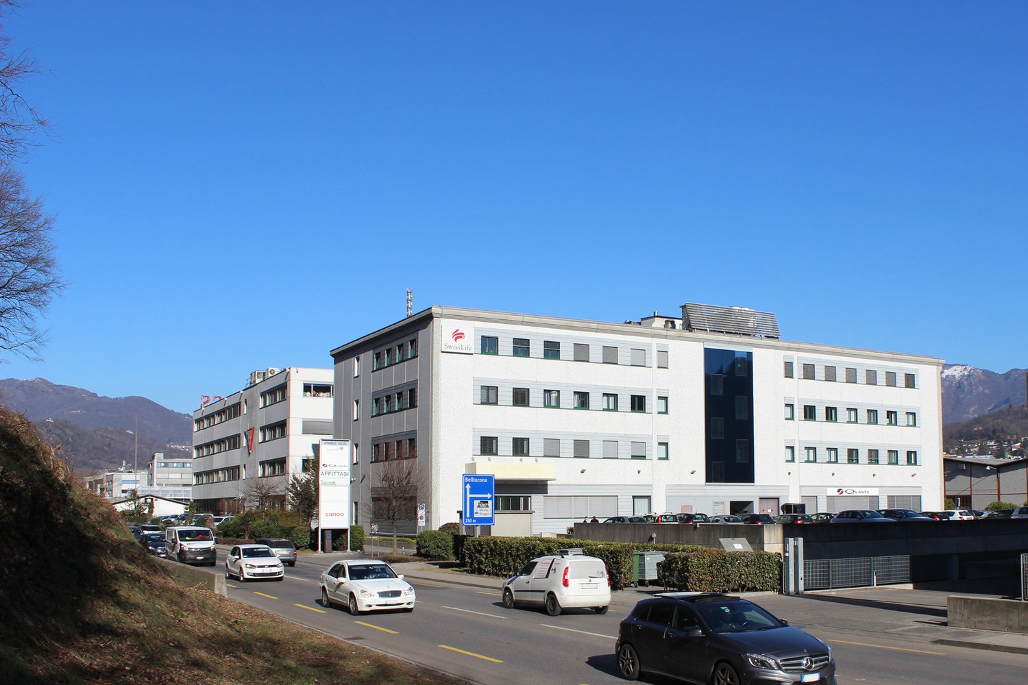 large white building, multiple windows, cars parked in front, mountains in the background